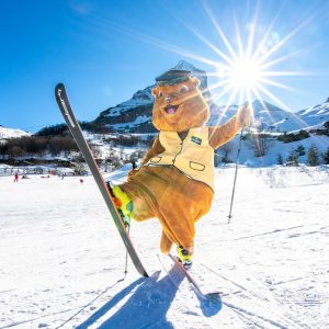 Gourette-Maskottchen auf Skiern. Hübscher orangefarbener Teddy mit Mütze