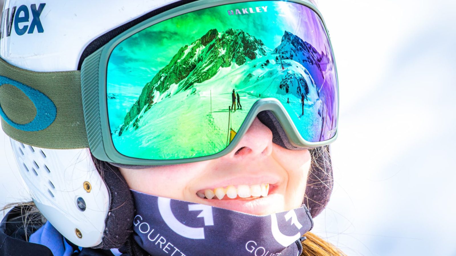 Portrait d'une jeune skieuse souriante portant un casque et un masque de ski aux couleurs bariolées.